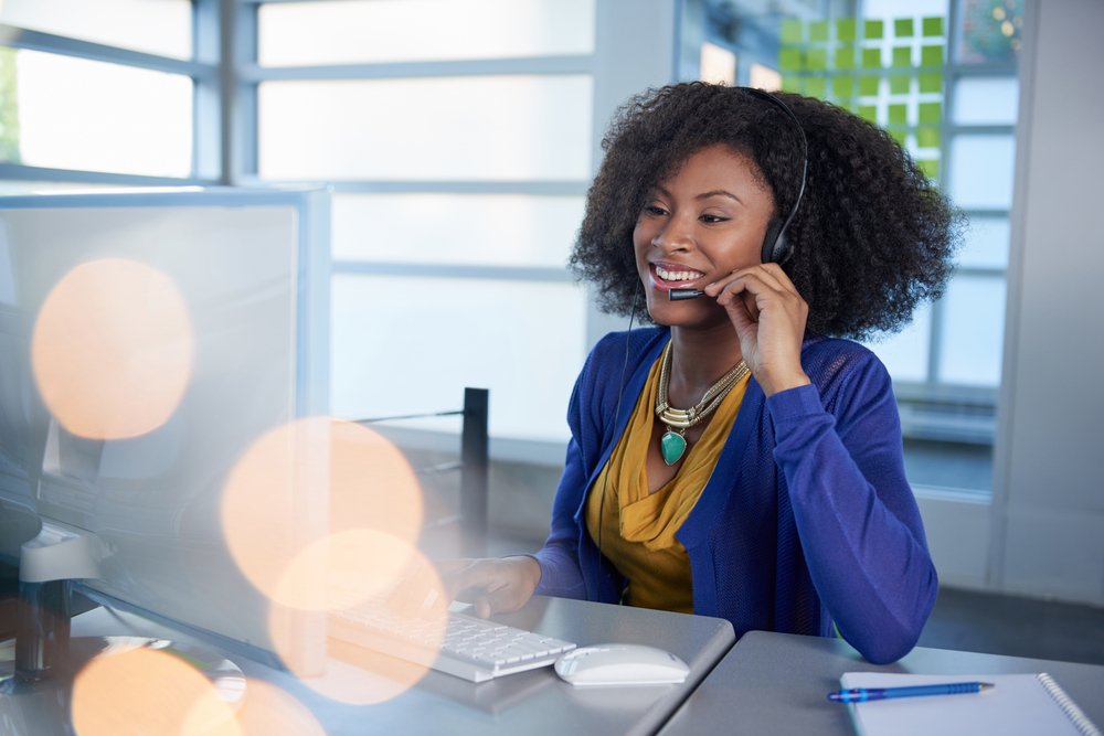 Portrait of a smiling customer service representative with an afro at the computer using headset-1 Portrait of a smiling customer service representative with an afro at the computer using headset-1